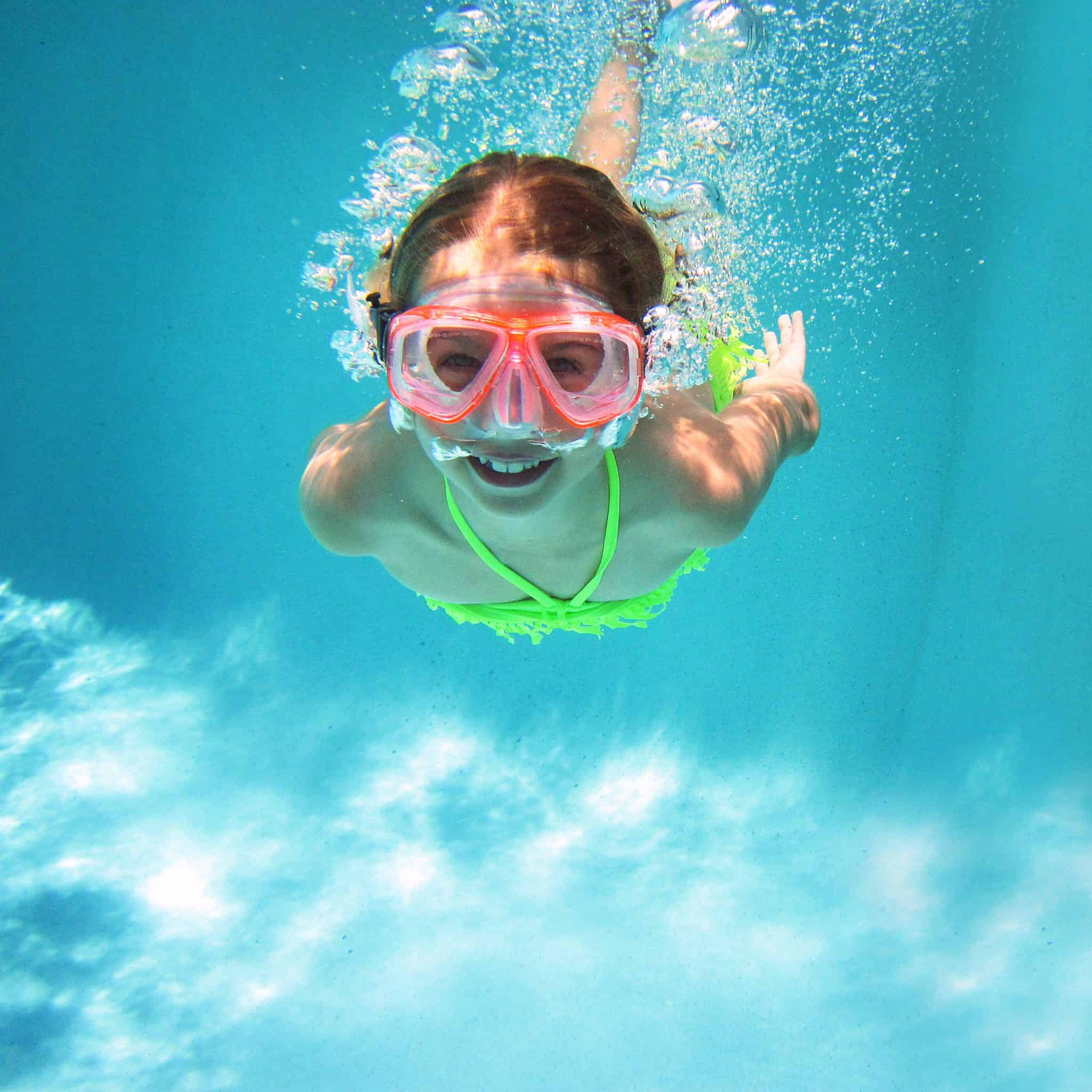 Girl in goggles swimming in a pool underwater and smiling