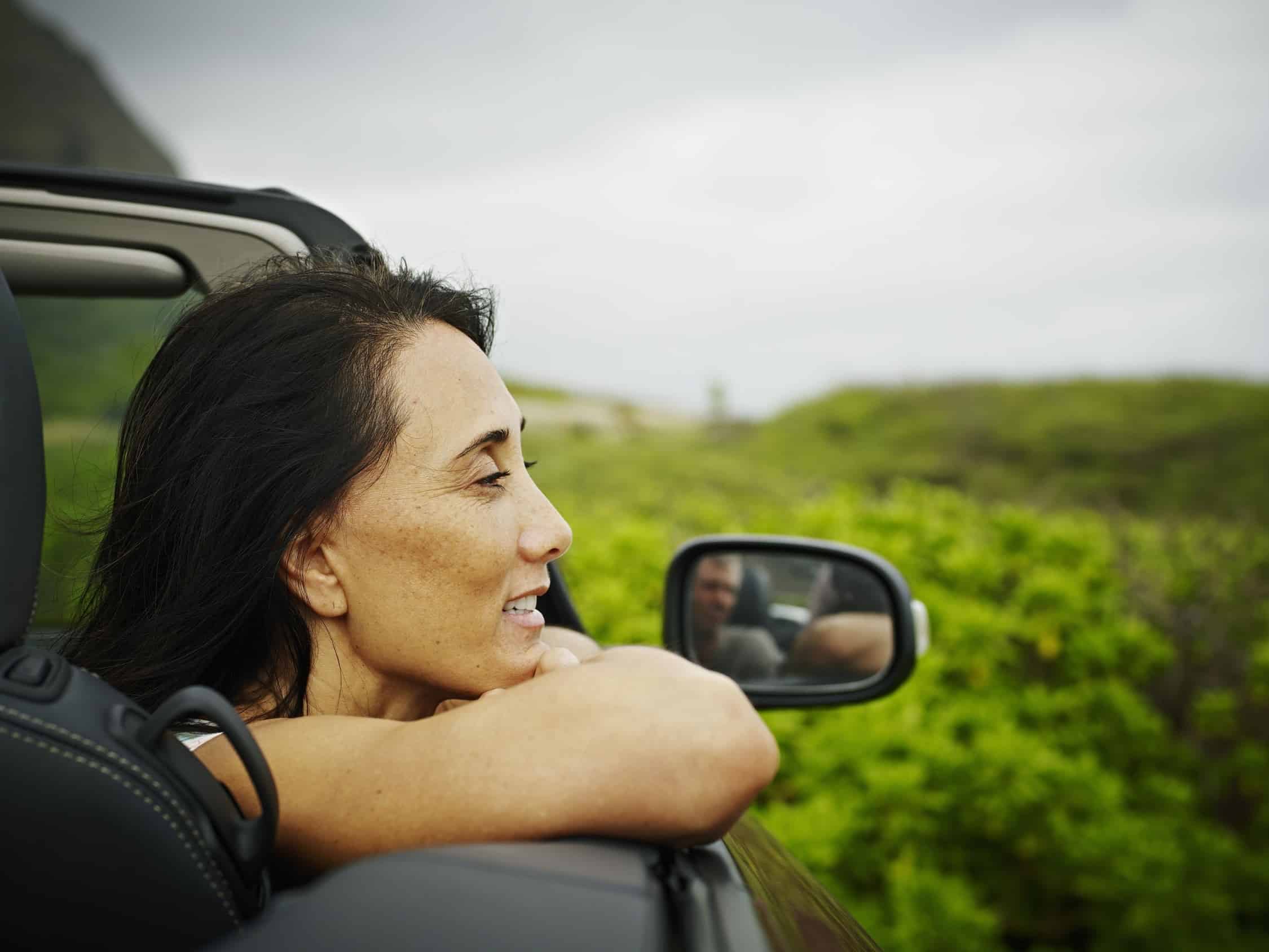 Profile of a woman leaning over the side of a convertible car